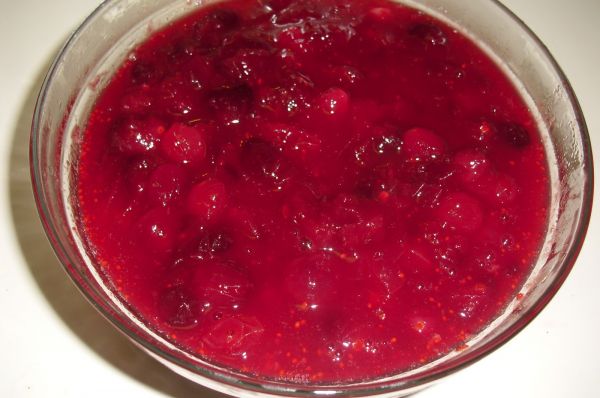 A bowl of homemade cranberry sauce, with whole crushed cranberries, served in a glass bowl.
