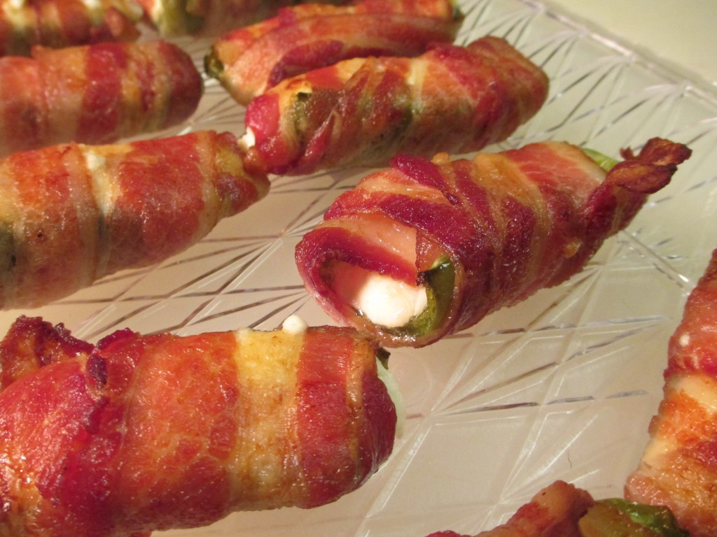 Rows of crispy and creamy bacon wrapped stuffed jalapeno poppers on a clear serving platter. 