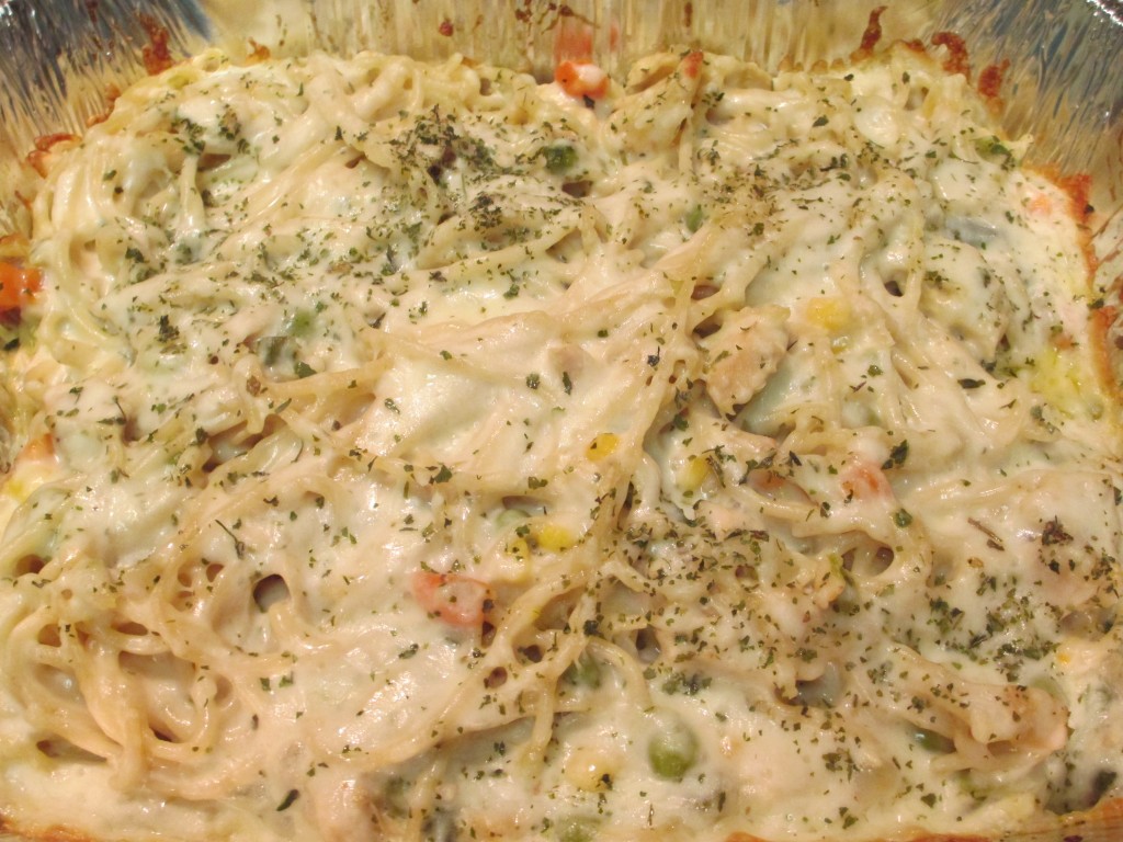 An aluminum pan filled with creamy Turkey Tetrazzini topped with melted cheese and sprinkled with parsley flakes.