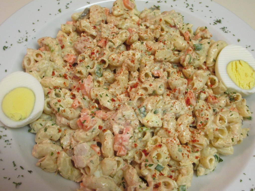 A close-up of a plateful of creamy tuna pasta salad sprinkled with paprika and garnished with a halved hardboiled egg, all on a round white plate.