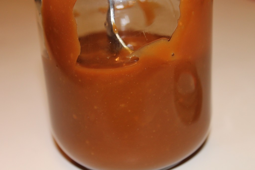 Golden salted caramel sauce in a glass jar. A spoon rests inside. 