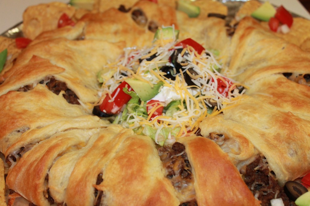 A close up of the middle of a golden Crescent Roll Taco Ring piled high with sour cream, veggies and shredded cheese. 