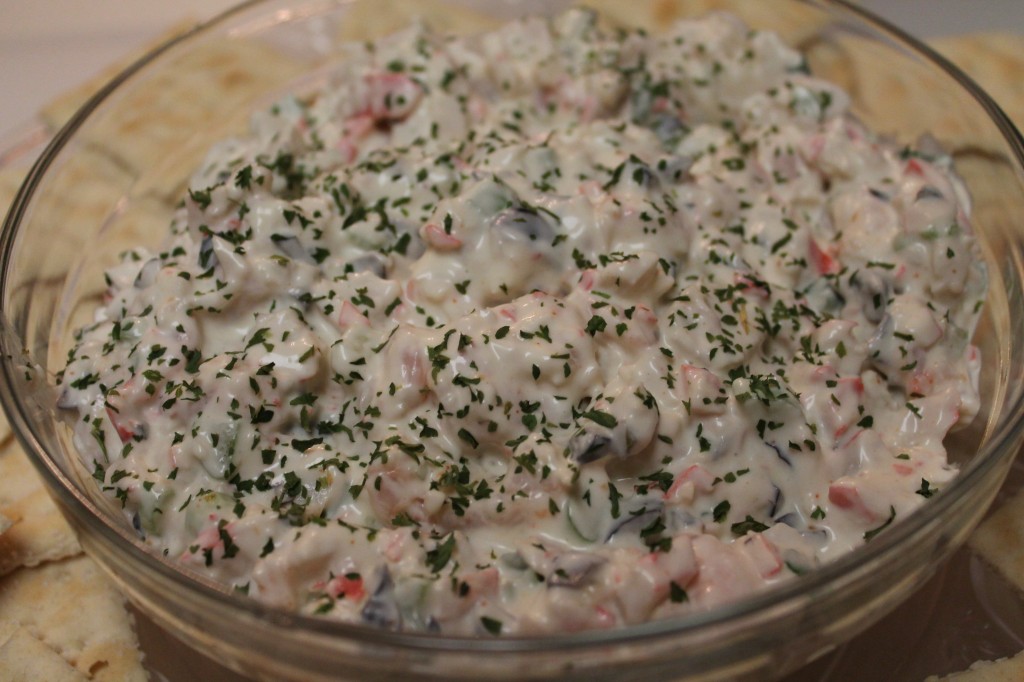 A close-up image of a large glass bowl filled with seafood salad. The simple salad is made with imitation crab, shrimp, and fresh veggies mixed in a creamy mayo-based dressing and garnished with parsley flakes.