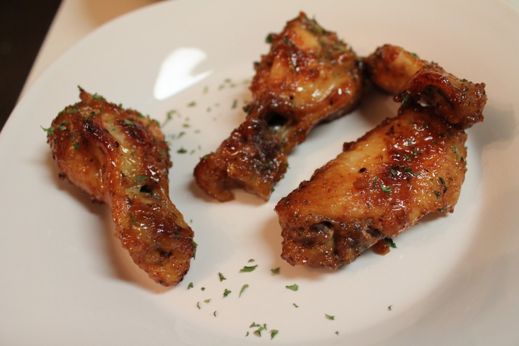 Four Basil Honey Mustard Wings garnished with dried basil on a round white plate.