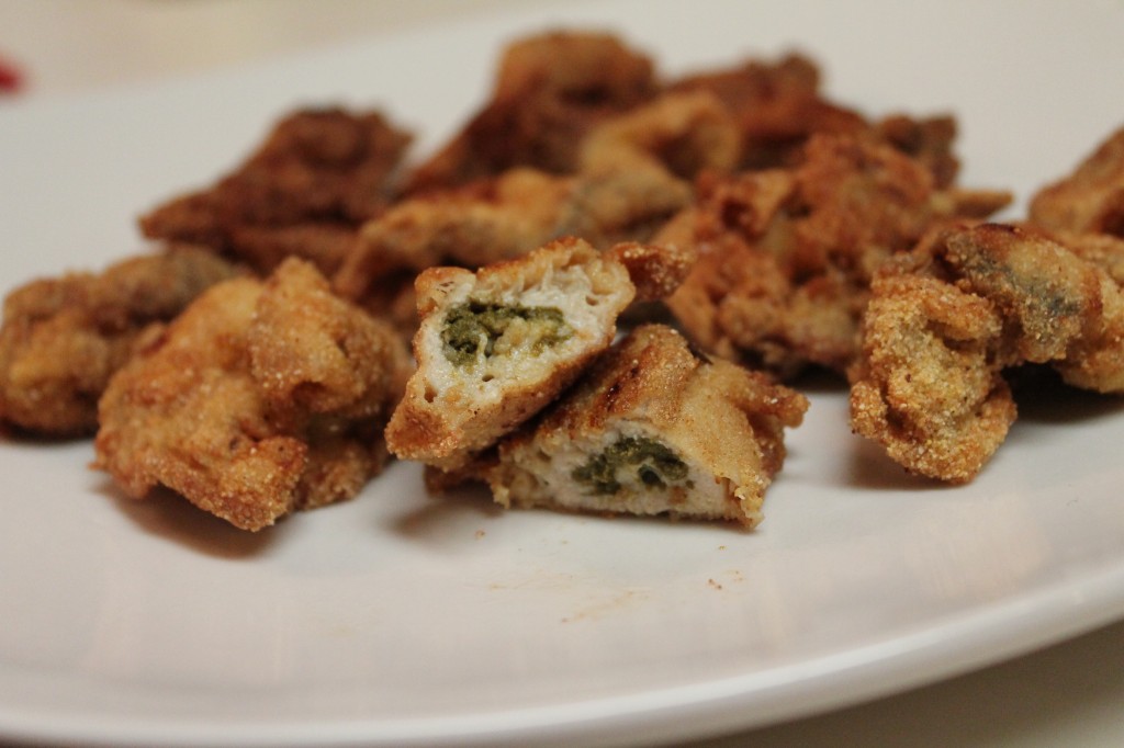 A tender fried oyster sliced in half alongside whole fried oysters all served on a white platter. 