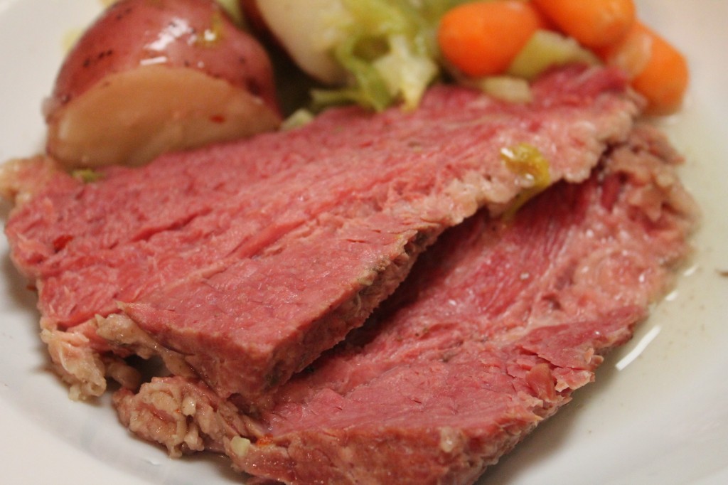 On a white plate, two slices of tender stovetop corned beef are served with cabbage, potatoes, and carrots.