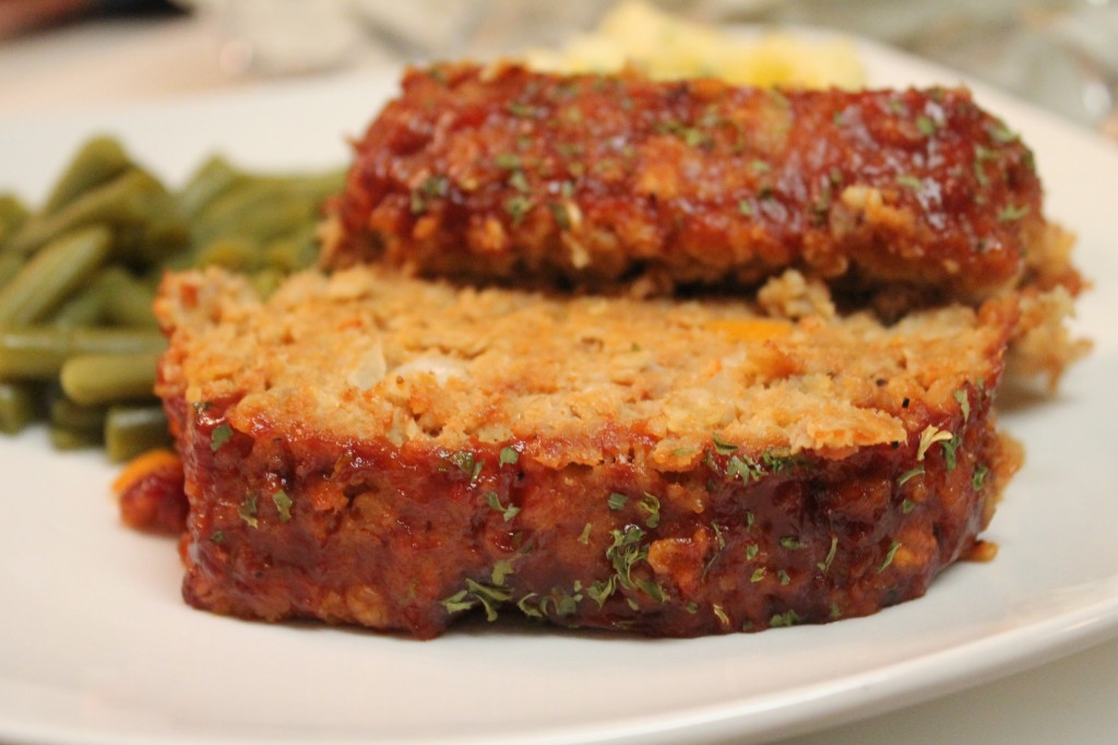 Two moist and tender slices of Turkey Meatloaf garnished with parsley served alongside green beans on a white plate. 