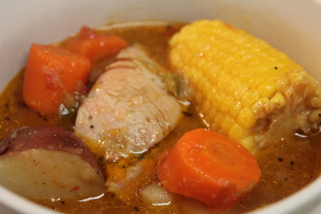 A white bowl filled with tender chicken, golden corn on the cob, bright carrots and creamy potatoes in a comforting broth. 