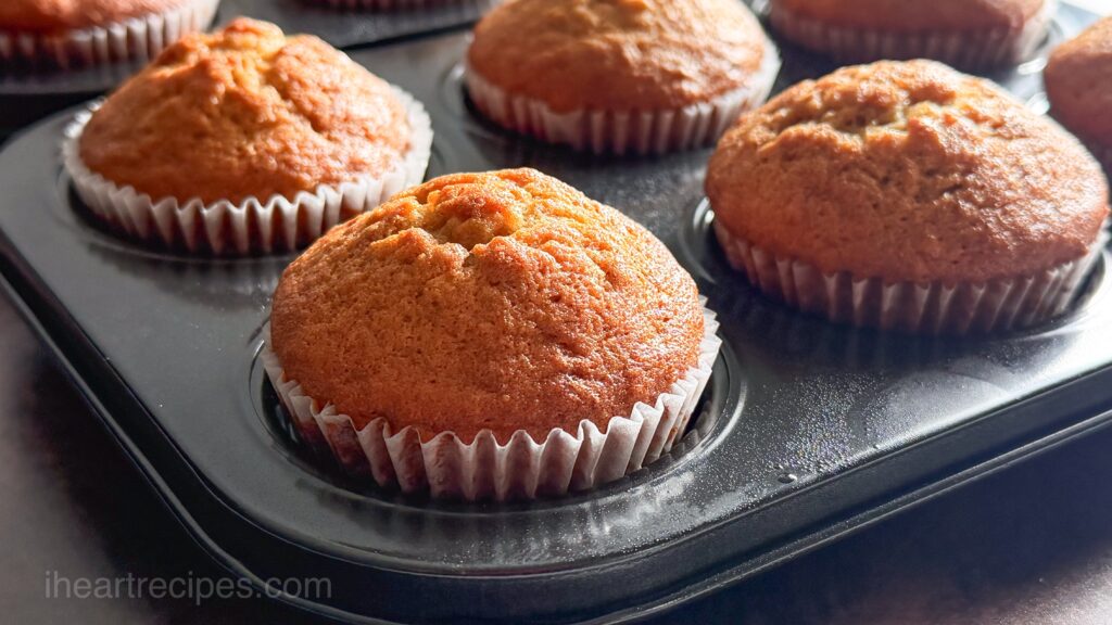 Freshly baked banana muffins cooling in a muffin tin pan.