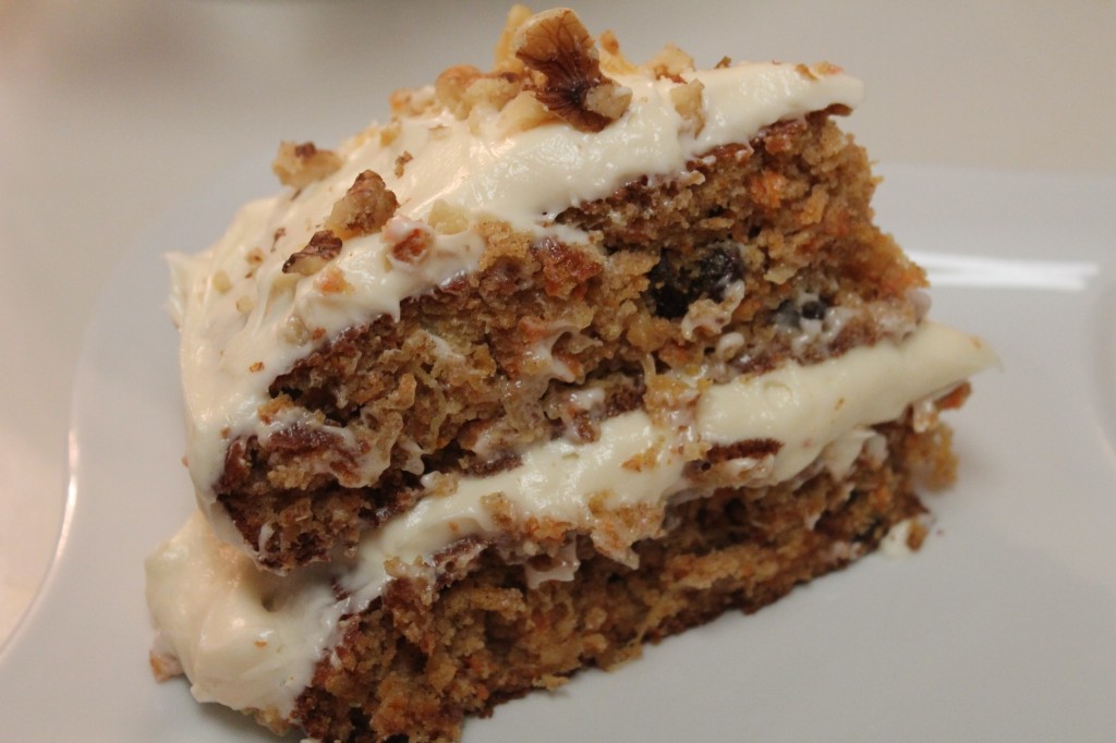 A slice of loaded carrot cake with gooey cream cheese frosting slathered on each layer. 