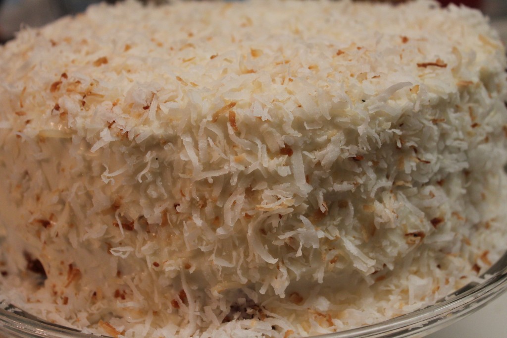 A moist and fluffy coconut cake topped with a sweet whipped frosting and toasted coconut shavings served on a glass cake platter. 