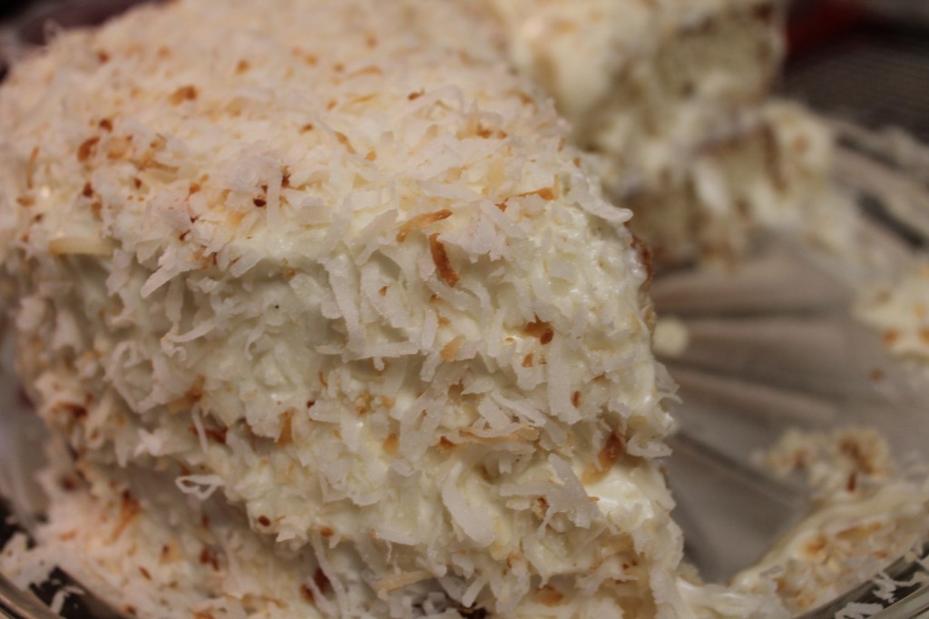 Sweet, moist white coconut cake with a homemade whipped cream icing and shaved toasted coconut flakes served on a glass platter. 