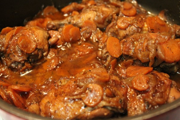 Delicious brown stewed chicken and carrots simmering in a large pot. 