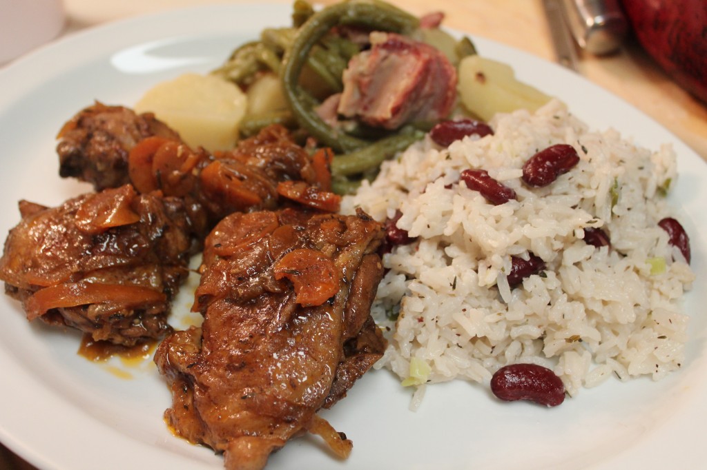 Brown stewed chicken and carrots served over rice and beans with potatoes and ham hocks on the side. 