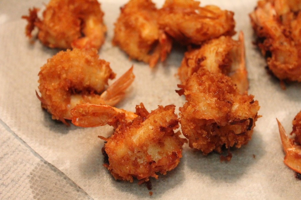 Golden and crispy fried coconut shrimp rest on a paper towel-lined platter. 