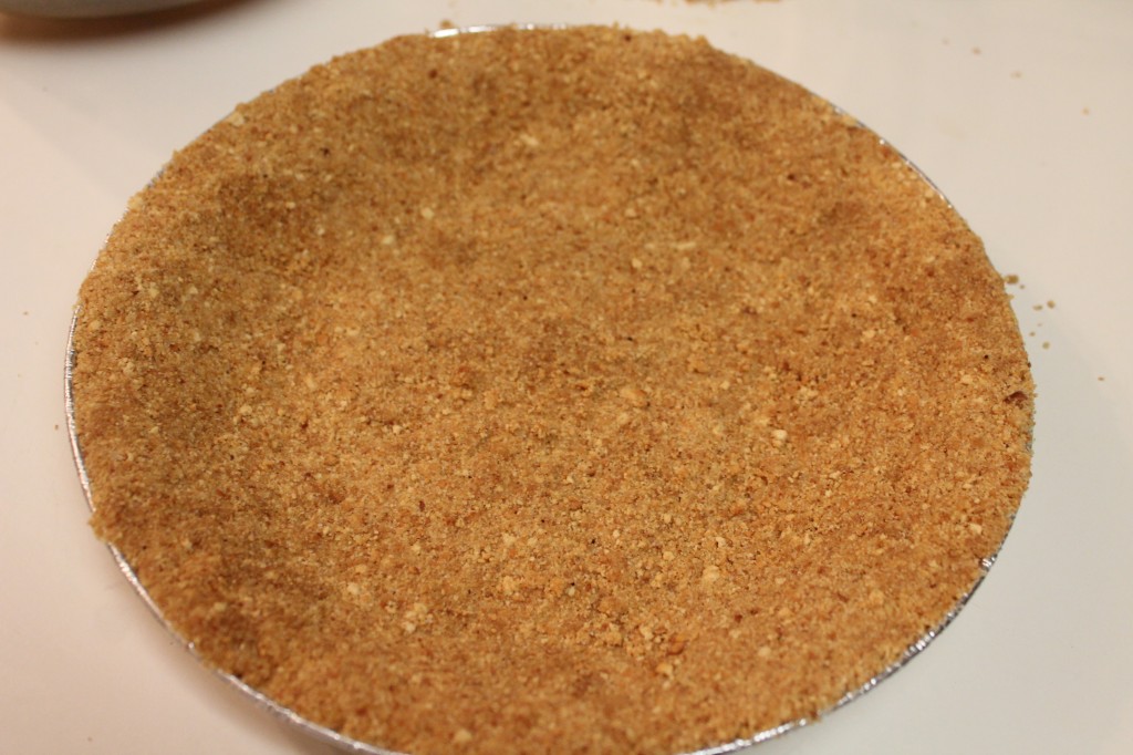 A graham cracker crust in a silver tin pie plate. 