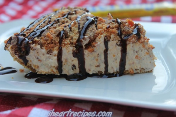 A slice of No Bake Butterfinger Pie drizzled with chocolate syrup sitting on a white plate. 