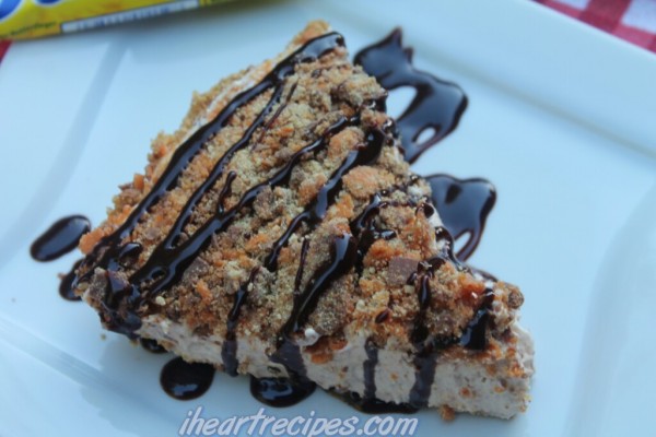 A slice of No Bake Butterfinger Pie drizzled with chocolate sauce on a white square plate. 