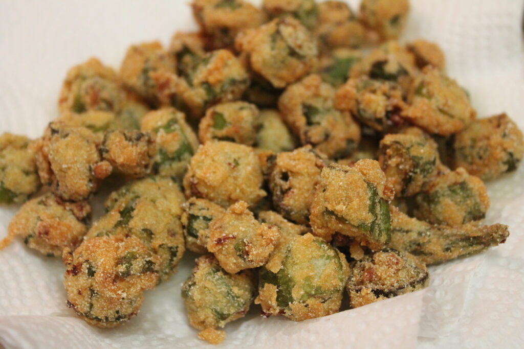 Pieces of crispy Southern fried okra coated in flour and cornmeal sitting on a paper towel to drain the excess oil.