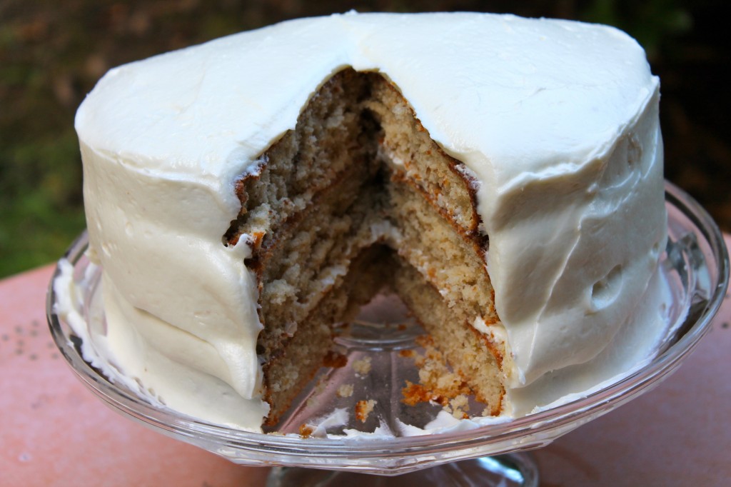 A picture-perfect Southern Hummingbird cake with a single slice cut out, revealing the moist triple layer spiced banana cake filled with homemade cream cheese icing.
