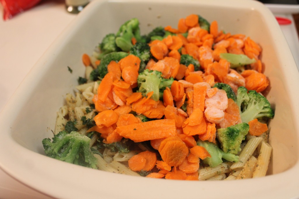 Seasoned, cooked pasta with frozen broccoli and carrots in a baking dish. 