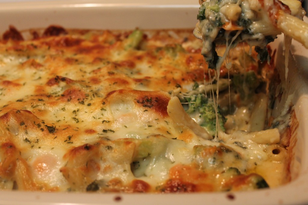 A cheesy spoonful of baked vegetable ziti being served from a panful of tender pasta and crisp veggies in a creamy cheese sauce.