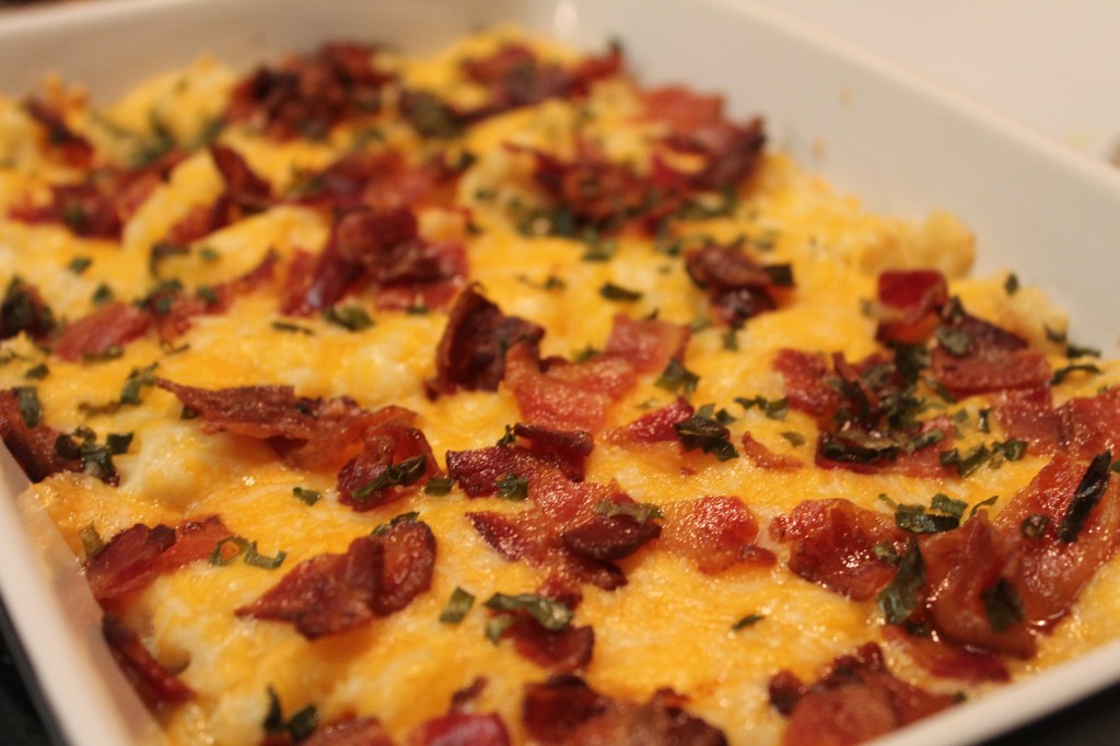 Twice baked potato casserole covered in gooey cheese, crispy bacon and bits of green onion served in a white casserole dish. 