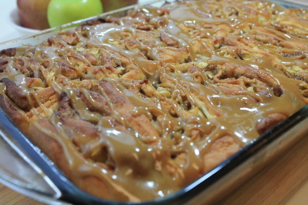 A glass bake dish filled with gooey caramel apple cinnamon rolls drizzled with a sweet golden glaze. 