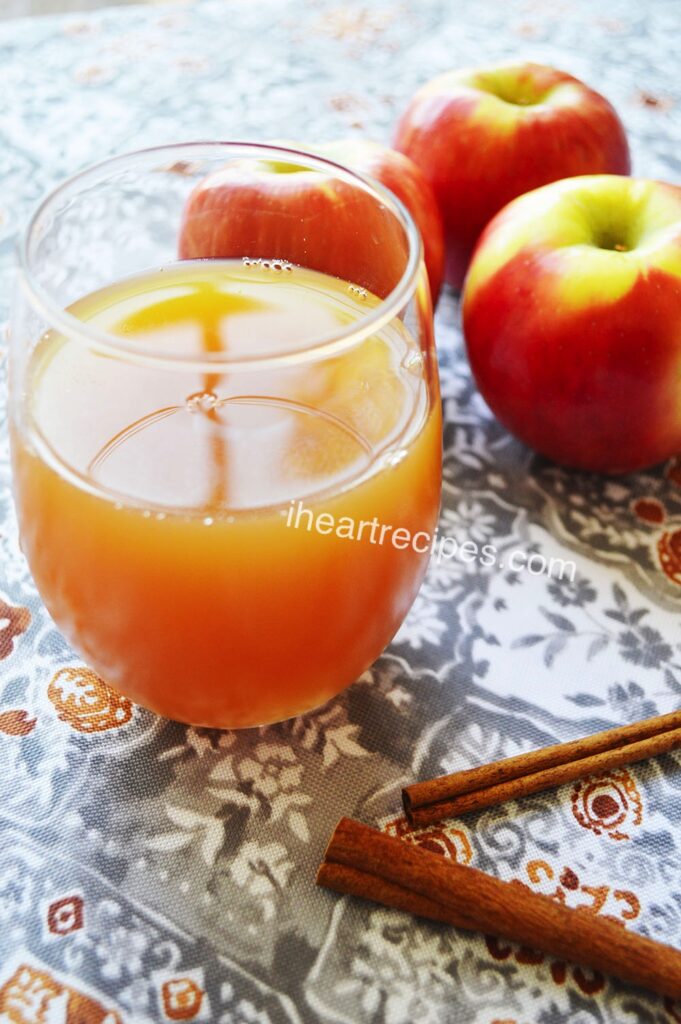 Homemade apple cider in a clear glass set on a grey and orange table cloth. 