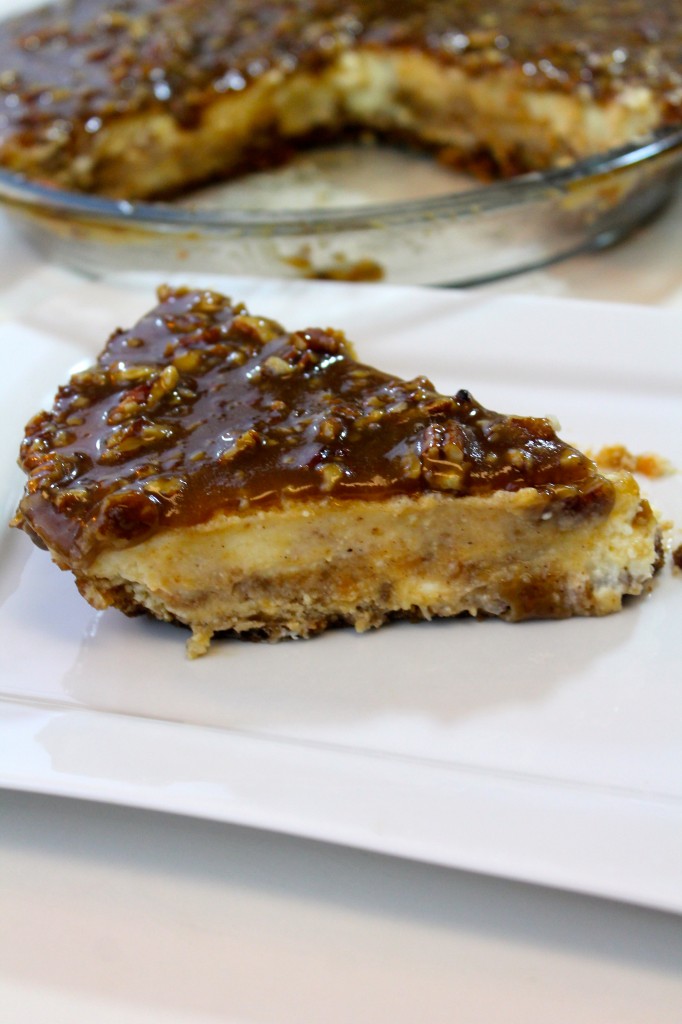 A slice of creamy Sweet Potato Cheesecake with praline topping on a square white dish. The remainder of the pie is in a glass dish in the background.