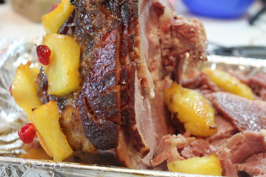 A classic spiral brown sugar glazed ham in a foil-lined pan. Pineapples with cherries are secured to the ham with toothpicks