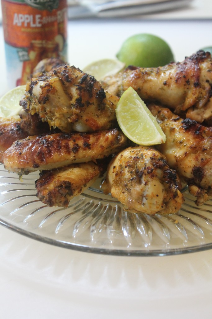 A glass plate piled high with Baked Cilantro Lime Chicken Wings and lime wedges. 