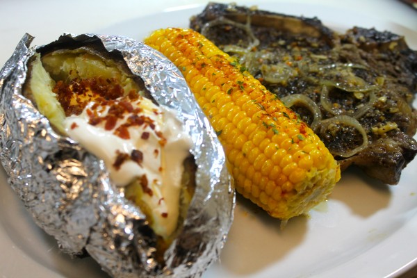 Garlic t-bone steak prepared with garlic, mushrooms, and onions and served with corn on the cob.