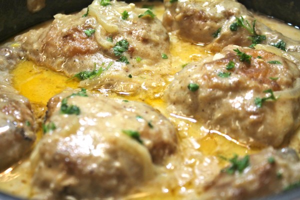 A close up of golden and juicy Smothered Southern Chicken in a black pan. 