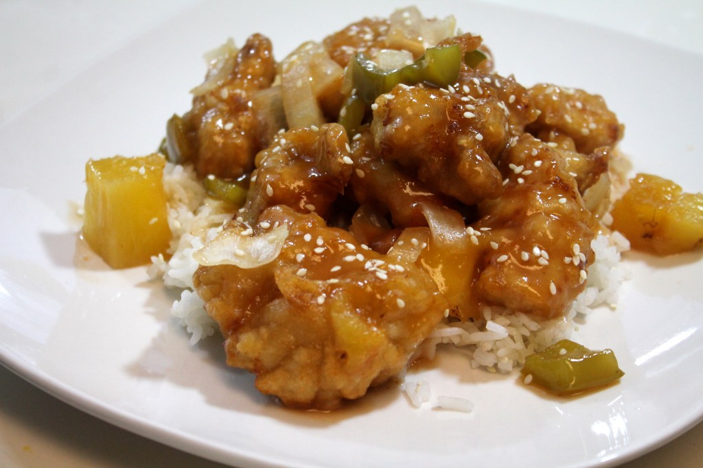 Golden sweet and sour chicken served over a bed of white rice and garnished with sesame seeds. 