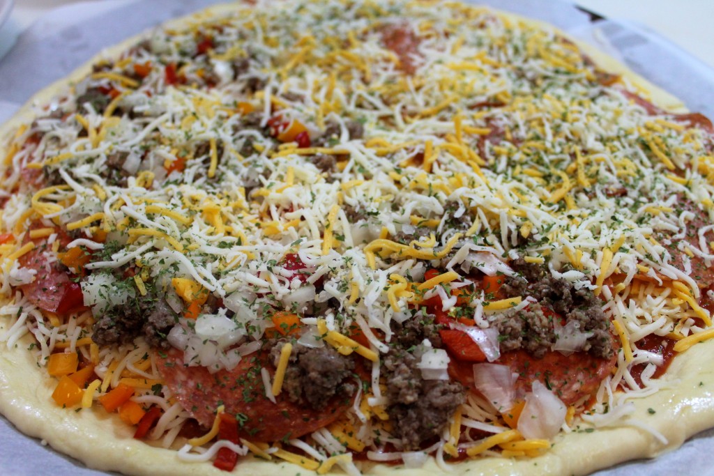 Pizza dough stacked high with a variety of pizza toppings ready to be baked. 