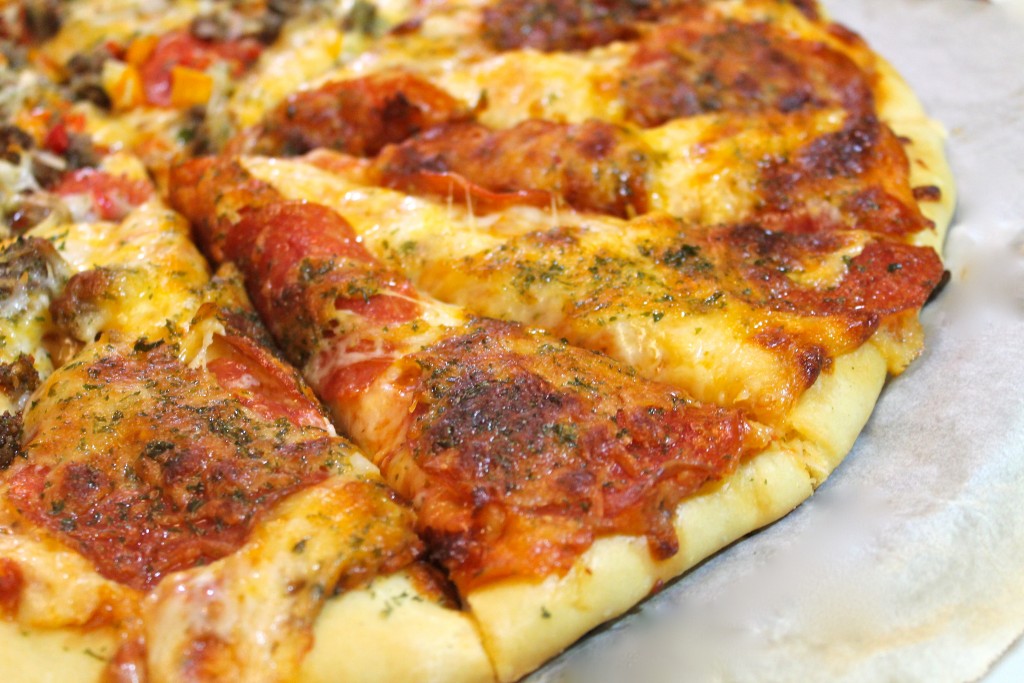 A close up of a parchment paper lined pizza pan with a cooked cheesy pepperoni pizza seasoned with Italian seasonings.