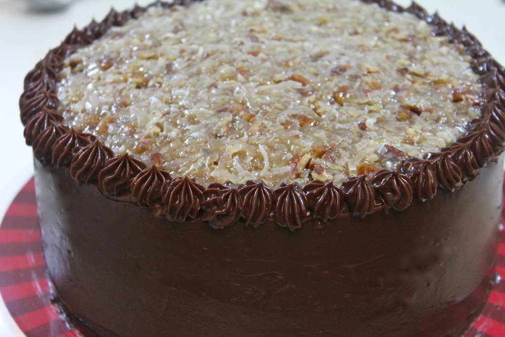 German chocolate cake with the sides frosted in a creamy dark chocolate frosting and topped with a sweet coconut pecan frosting served on a red and maroon striped platter. 