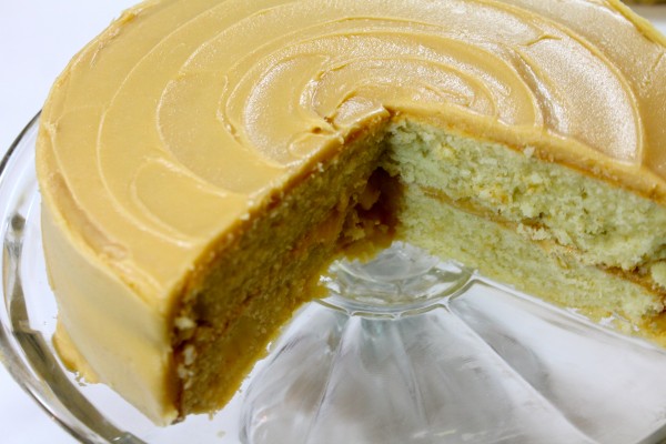 A deliciously moist Southern Caramel cake sits on a glass cake platter with two large slices cut out. The cake is frosted with a decadent caramel icing, and the inside is a moist homemade yellow cake.