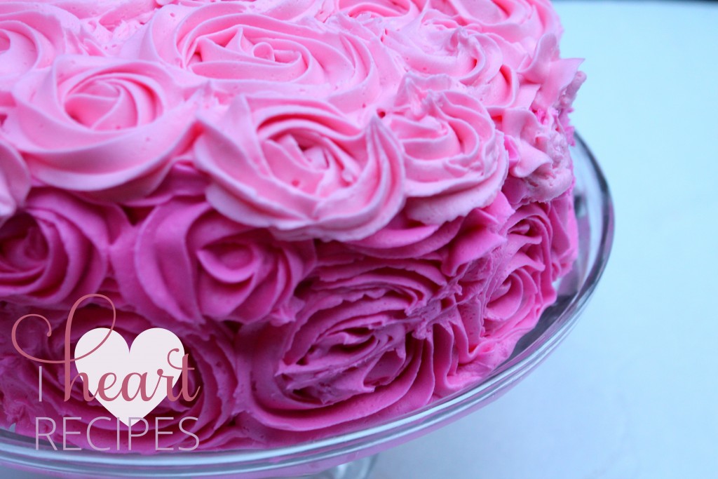 Pink ombre rose swirls embellish a round cake on a glass cake stand. 