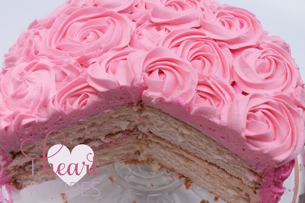 A sliced, two-layer, moist vanilla cake decorated with pink frosting rose swirls on a glass cake stand.