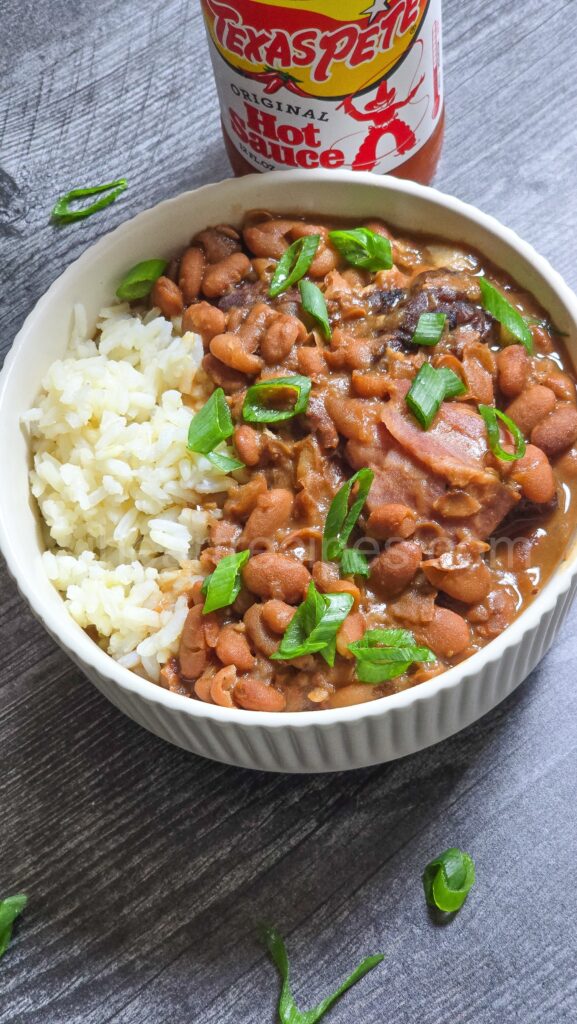 hearty beans and rice in a bowl, with a bottle of hot sauce.