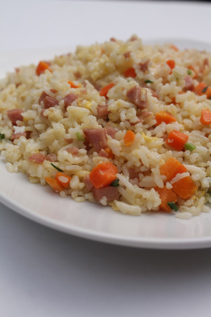 A white bowl full of golden fried rice mixed with tender ham and diced carrots.  