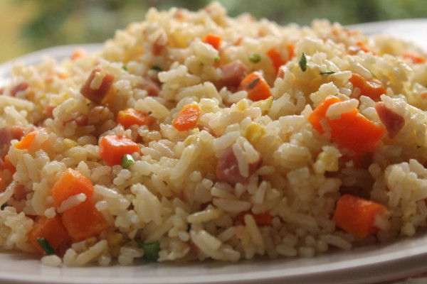 A close-up image of fried rice speckled with bright orange carrots, tender ham pieces, golden egg bits and garnished with fresh green herbs. 