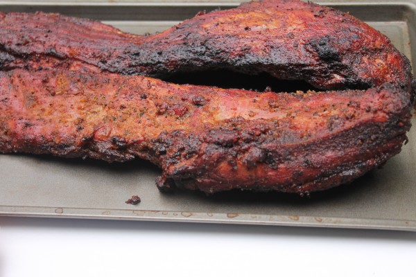 Two slabs of cooked rib tips rest on a metal baking sheet. The ribs have a flavorful crust of seasonings and dry-rub sauce with bits of char from the grill.