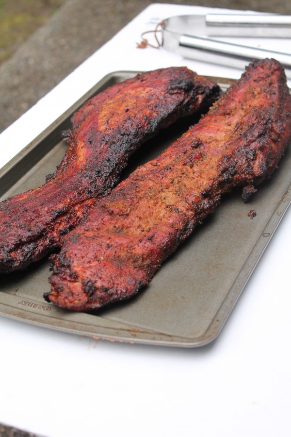 Two slabs of grilled rib tips rest on a baking sheet. The ribs have bits of char around the edges and are covered with a zesty BBQ seasoning mix.