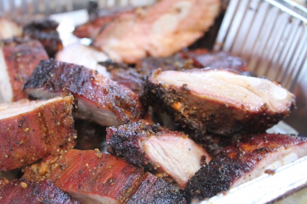 Tender and juicy BBQ rib tips rest in an aluminum pan. The rib tips have a char-cooked outer seasoning crust and are moist and juicy in the center.