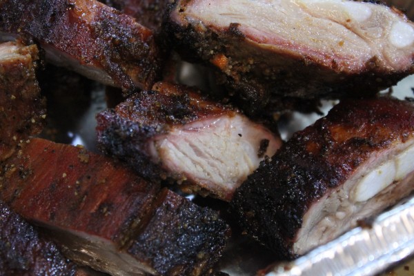 A closeup image of grilled BBQ rib tips cut into small pieces in an aluminum container. The outside of the rib tips has a smoky black crust with layers of seasonings and spices.