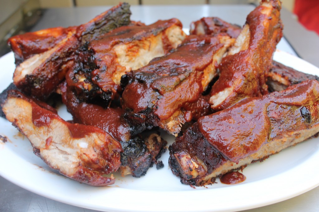 St. Louis style ribs drenched in sauce and piled on a white serving platter. 