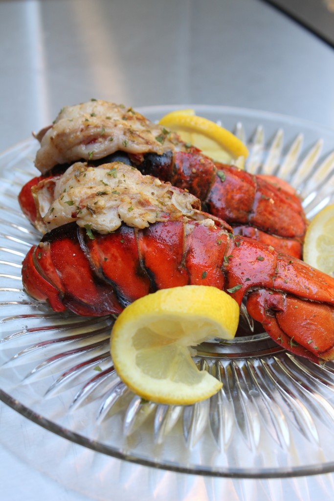 Grilled Lobster Tail on a clear glass plate served with lemon wedges. 